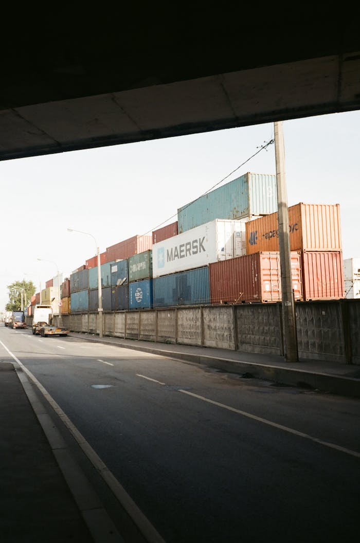 About Multicolored cargo containers stacked beside a busy urban street under a clear sky.