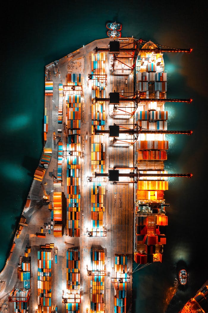 Home Dramatic aerial view of a busy shipping port with colorful containers and bright lights at night.