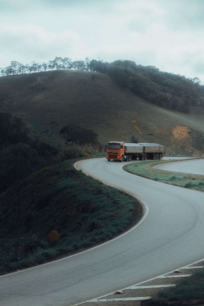 Home A red truck drives on a winding road in a mountainous landscape, showcasing scenic transportation.
